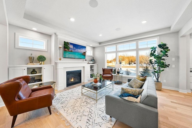 living room with baseboards, a glass covered fireplace, a healthy amount of sunlight, and wood finished floors