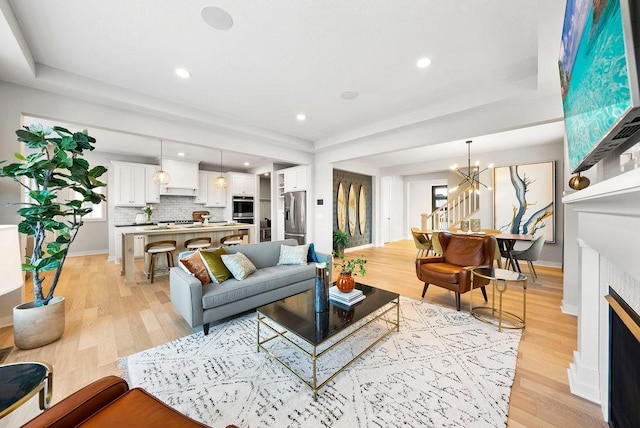 living area with light wood-style flooring, a notable chandelier, and a raised ceiling