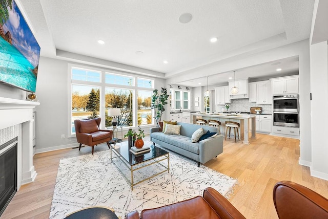 living area featuring baseboards, light wood-type flooring, recessed lighting, and a glass covered fireplace