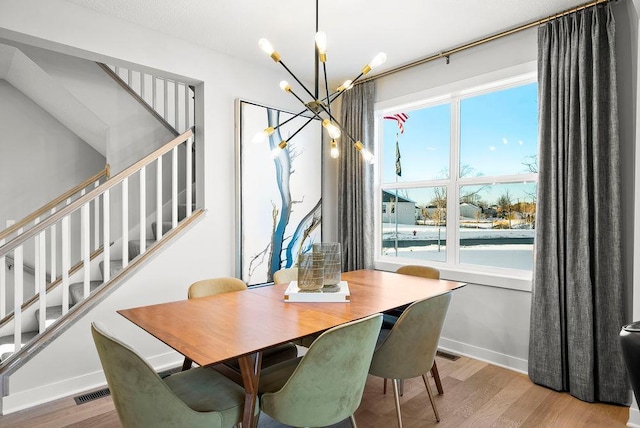 dining room featuring visible vents, baseboards, wood finished floors, stairway, and an inviting chandelier
