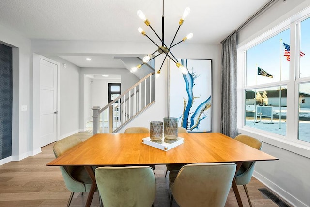 dining space with wood finished floors, a healthy amount of sunlight, stairway, and a notable chandelier