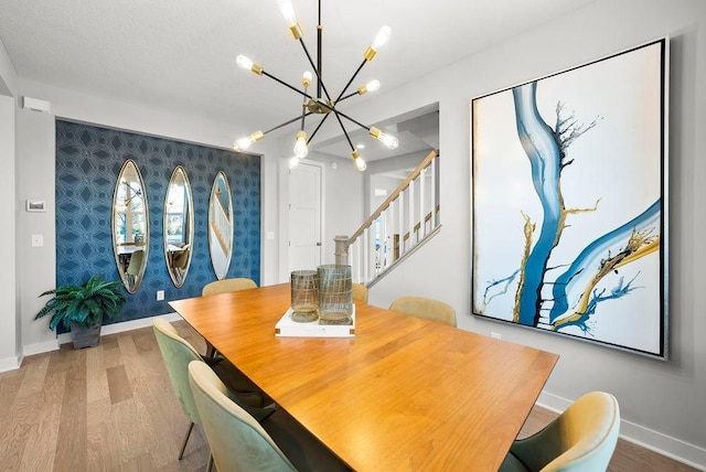 dining space featuring wallpapered walls, an accent wall, an inviting chandelier, and wood finished floors