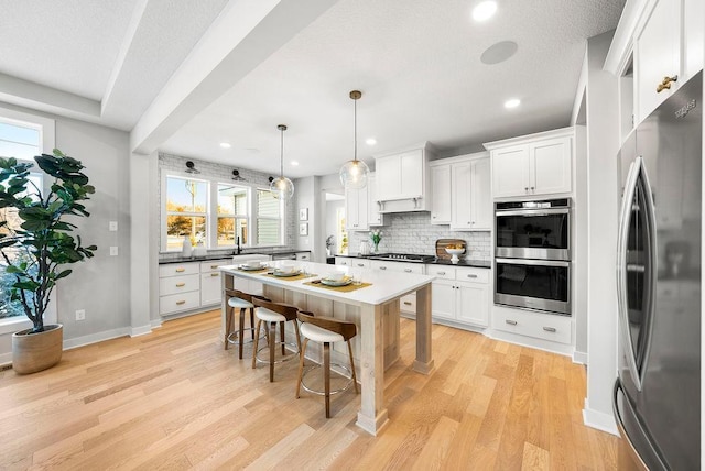kitchen featuring a kitchen breakfast bar, tasteful backsplash, stainless steel appliances, light wood finished floors, and white cabinets