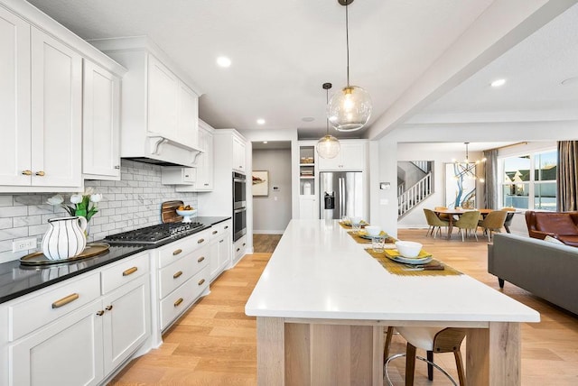 kitchen featuring light wood-type flooring, a center island, decorative backsplash, white cabinets, and appliances with stainless steel finishes