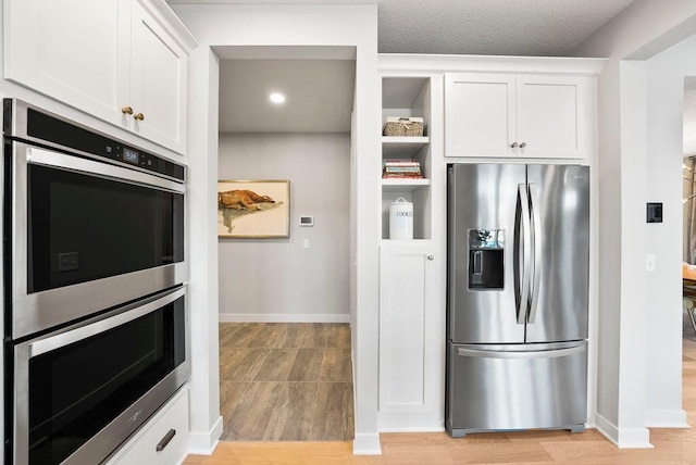 kitchen with baseboards, white cabinetry, stainless steel appliances, and light wood-style floors