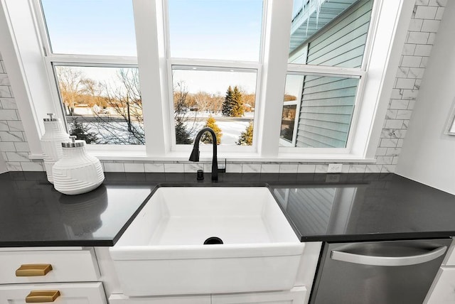 interior details featuring tasteful backsplash, stainless steel dishwasher, a sink, dark countertops, and white cabinets