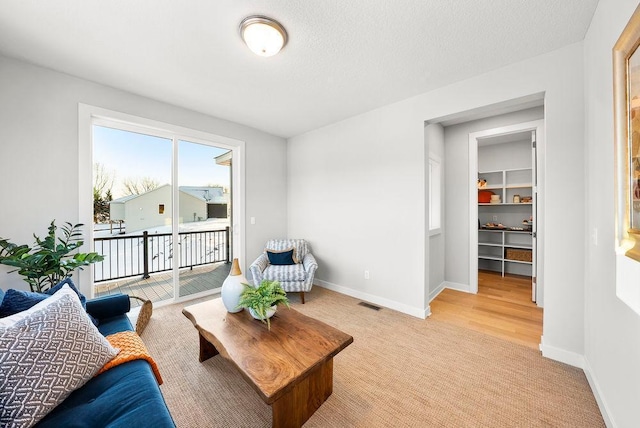 living area featuring visible vents, baseboards, light colored carpet, and a textured ceiling