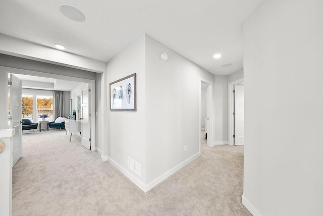 hall with light carpet, baseboards, and visible vents