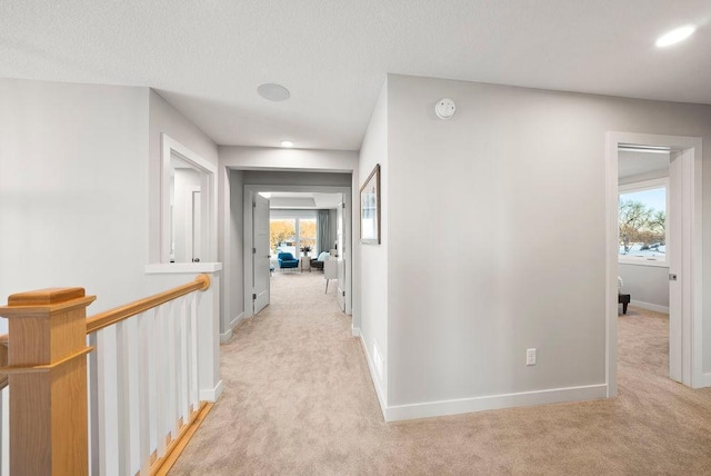 corridor featuring baseboards, a textured ceiling, an upstairs landing, and light carpet