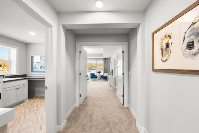hallway featuring a sink, light carpet, and baseboards