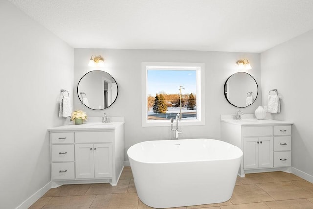 full bath with a sink, a freestanding tub, two vanities, and baseboards