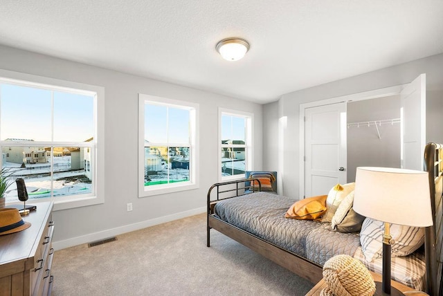 bedroom featuring a closet, baseboards, multiple windows, and light colored carpet