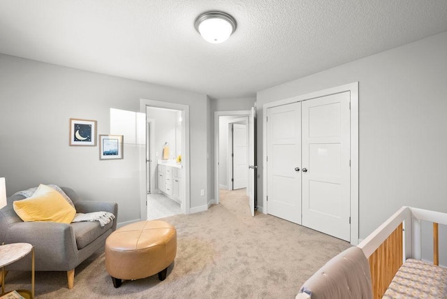 bedroom with connected bathroom, a closet, light carpet, a textured ceiling, and baseboards