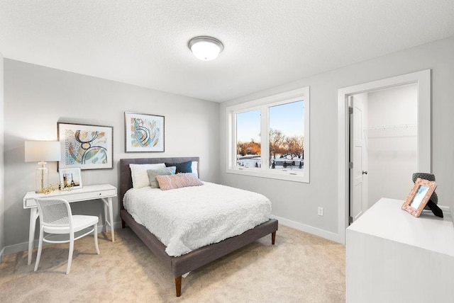 bedroom with a closet, a textured ceiling, baseboards, light carpet, and a spacious closet
