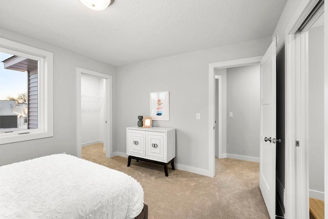 bedroom with a closet, a textured ceiling, baseboards, and light carpet