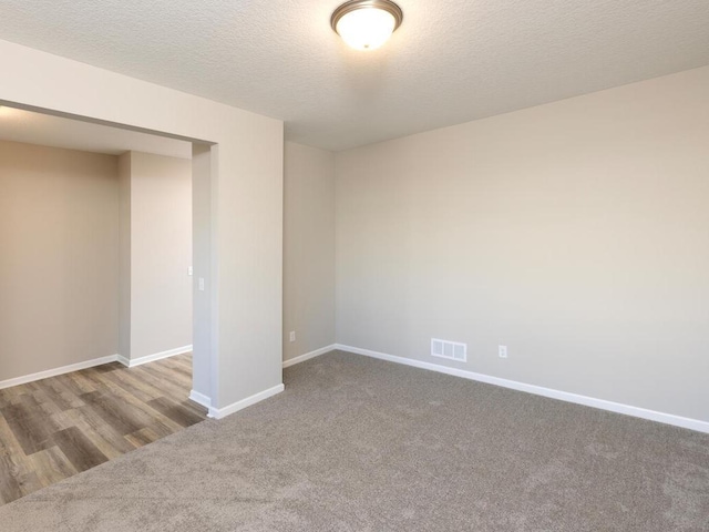 empty room with visible vents, baseboards, carpet, and a textured ceiling