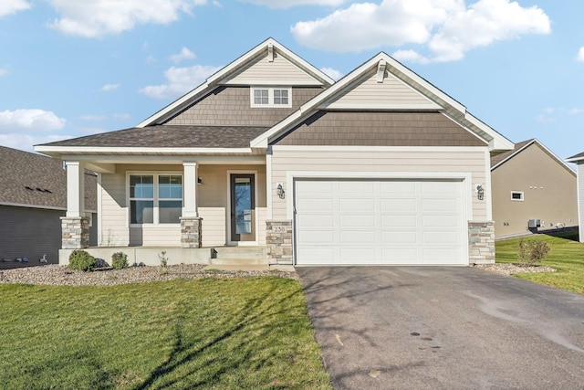 craftsman-style home featuring stone siding, aphalt driveway, a garage, a front yard, and a porch