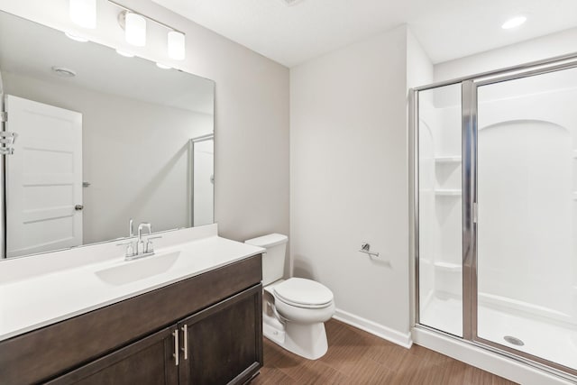 bathroom with vanity, toilet, baseboards, a shower stall, and wood finished floors