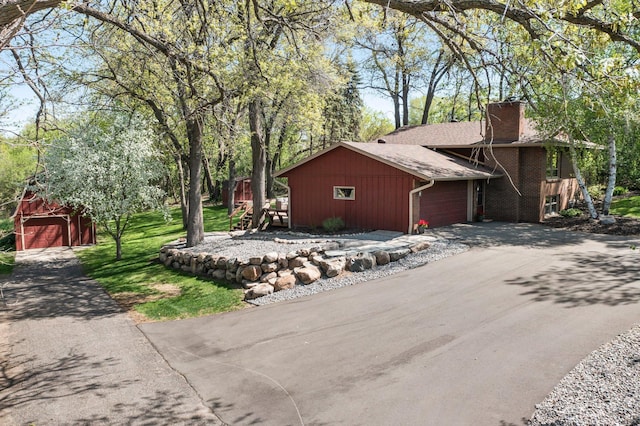 view of side of home featuring a chimney, driveway, a shingled roof, and a garage