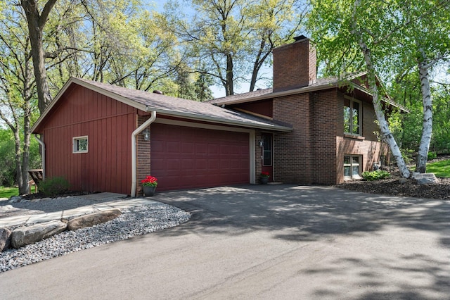 view of side of home featuring a chimney, brick siding, asphalt driveway, and a garage