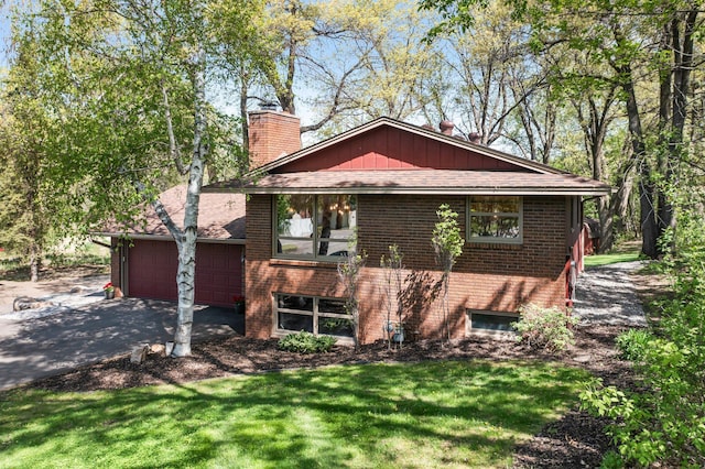 view of front of home featuring a chimney, brick siding, driveway, an attached garage, and a front yard