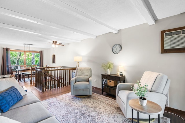 living room with beam ceiling, wood finished floors, a wall unit AC, a textured ceiling, and ceiling fan