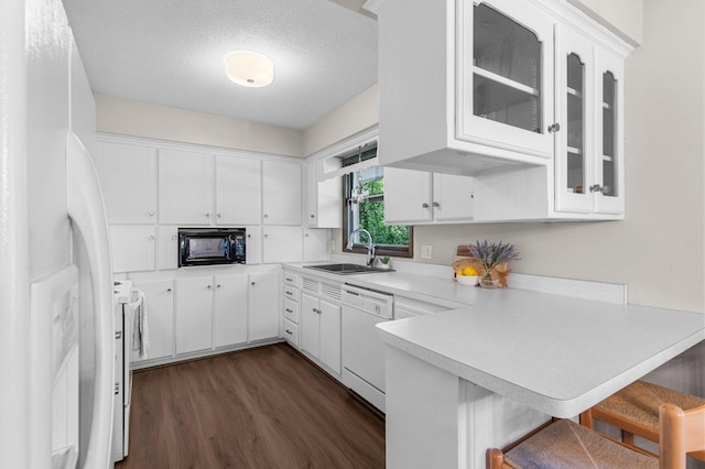 kitchen with a sink, white appliances, a peninsula, dark wood-style flooring, and light countertops