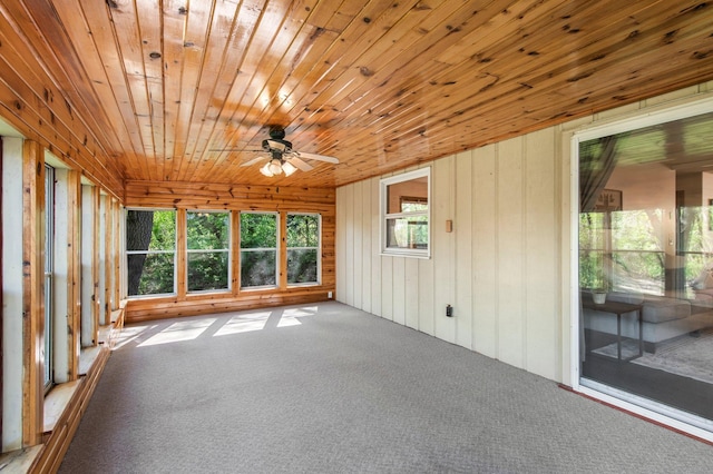 unfurnished sunroom with carpet flooring, a ceiling fan, wooden walls, and wood ceiling