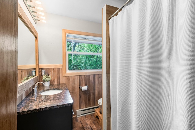 full bath with a baseboard heating unit, toilet, vanity, wood finished floors, and wainscoting