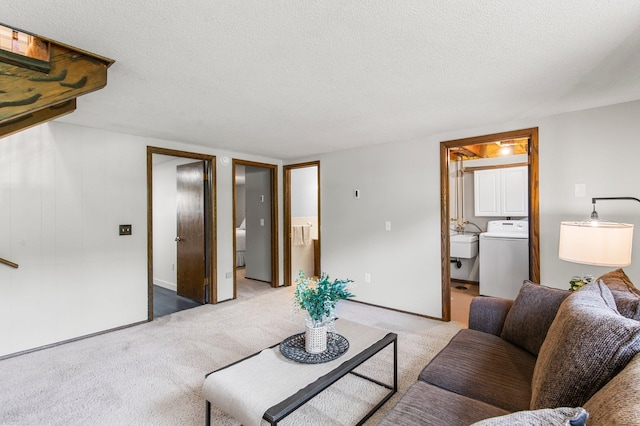 living room featuring washer / clothes dryer, light colored carpet, and a textured ceiling