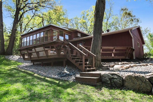 back of house featuring stairs, a wooden deck, a sunroom, and a lawn