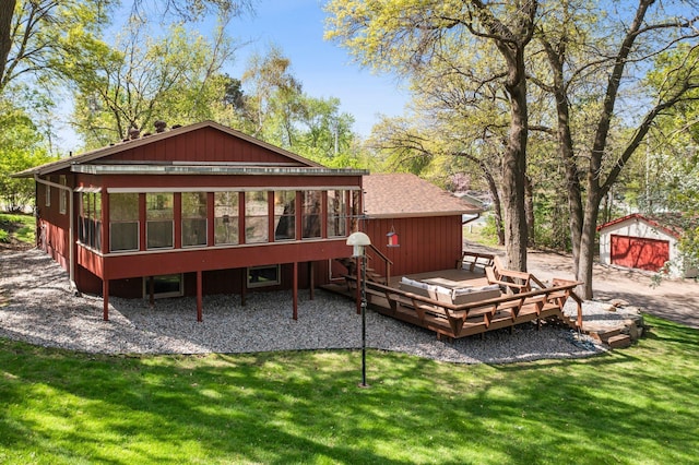 back of property with a deck, a sunroom, a yard, roof with shingles, and an outbuilding