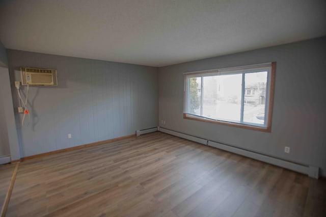 unfurnished room featuring a wall mounted air conditioner, a baseboard heating unit, baseboards, and wood finished floors