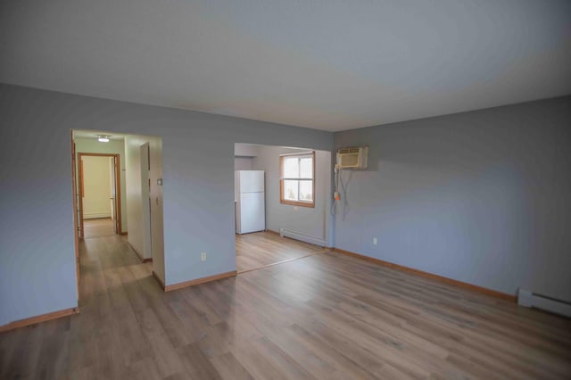 spare room with a baseboard radiator, light wood-style floors, a wall mounted AC, and baseboards