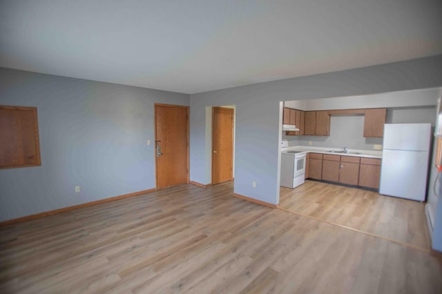 kitchen with a sink, light countertops, white appliances, brown cabinetry, and light wood-style flooring