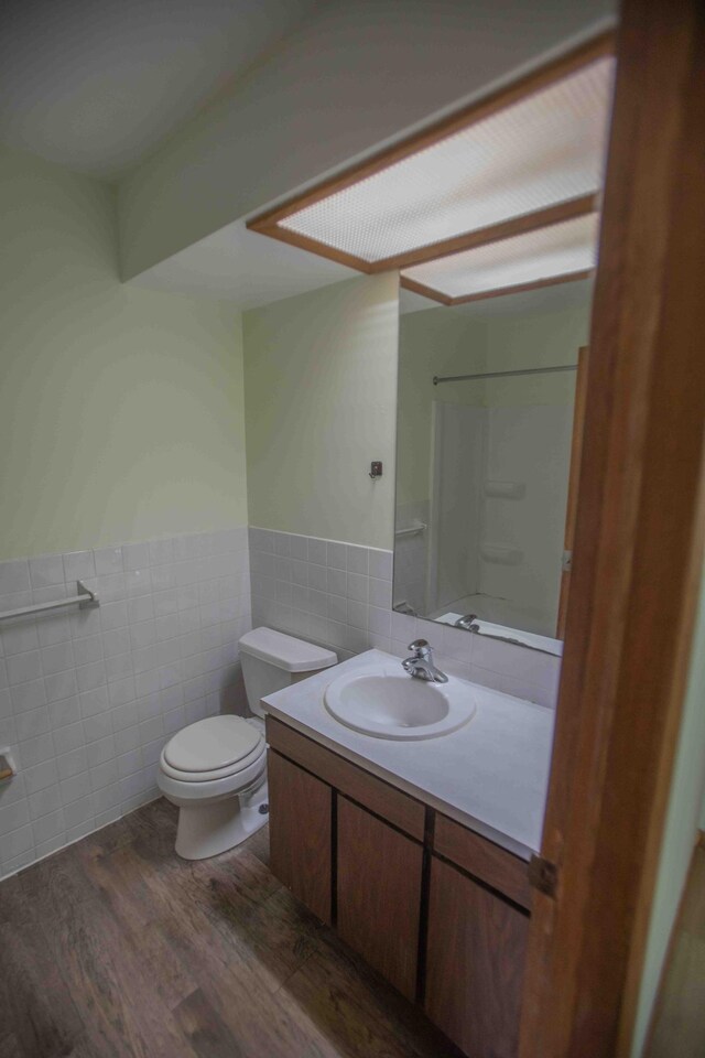 full bath with wainscoting, tile walls, toilet, and wood finished floors