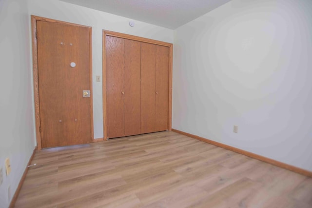 unfurnished bedroom with light wood-style flooring, a closet, and baseboards