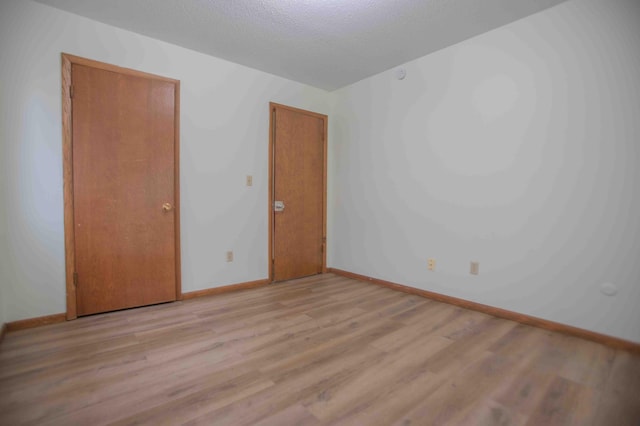 unfurnished room with light wood-style floors, baseboards, and a textured ceiling