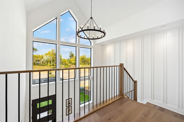 interior space featuring an inviting chandelier, high vaulted ceiling, a decorative wall, and wood finished floors