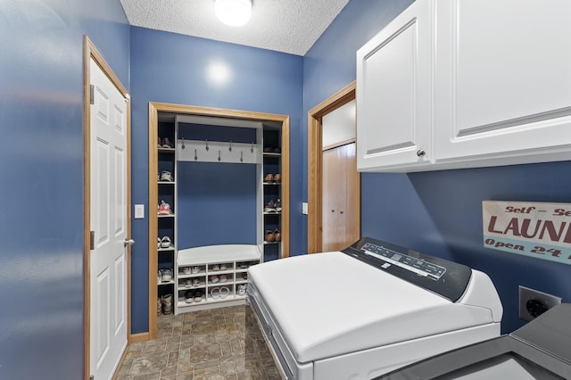 washroom with a textured ceiling, cabinet space, and washing machine and clothes dryer