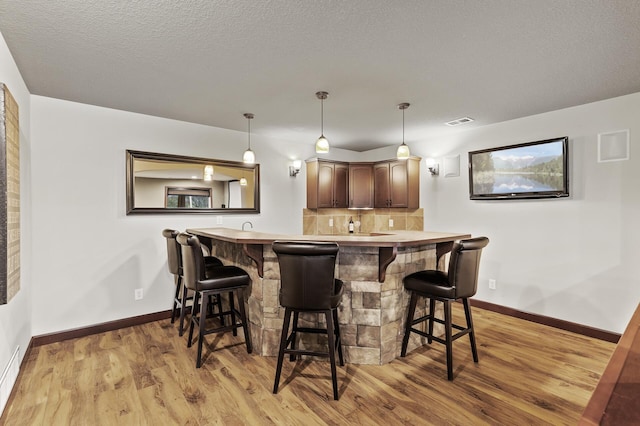 bar featuring pendant lighting, baseboards, light wood-type flooring, and visible vents