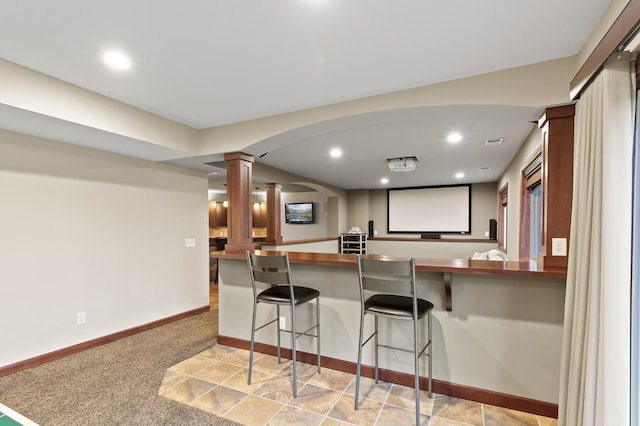 kitchen featuring decorative columns, a kitchen bar, arched walkways, baseboards, and recessed lighting