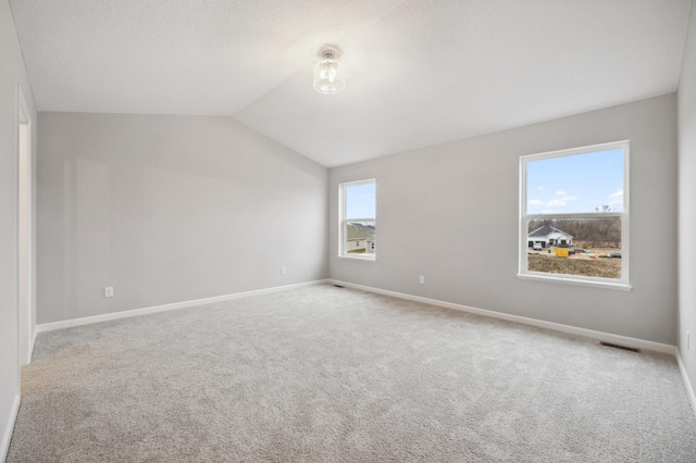 empty room with carpet flooring, visible vents, baseboards, and lofted ceiling