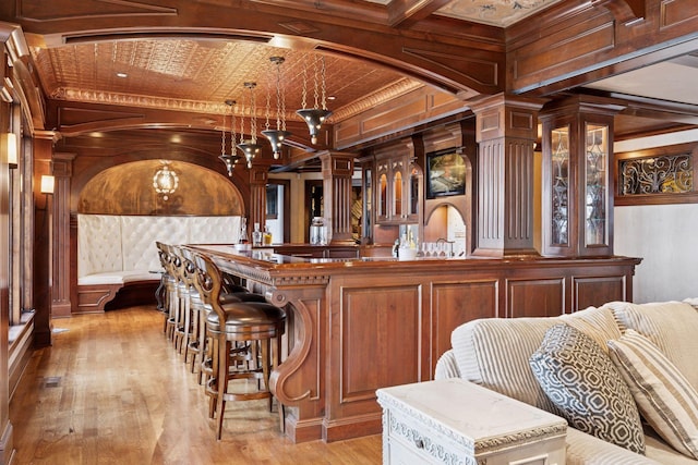 6425 Virginia Dr, Victoria, MN 55331 - bar area with light wood-style floors, ornate columns, wood walls, hanging light fixtures, and crown molding