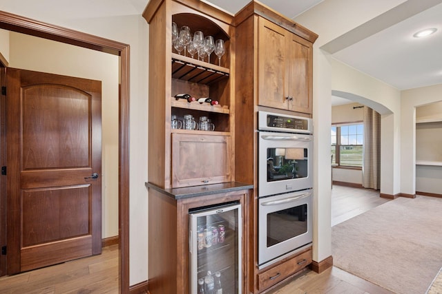 21804 Majestic Dr, Saint Augusta, MN 55320 - kitchen featuring light wood-style floors, stainless steel double oven, arched walkways, baseboards, and wine cooler