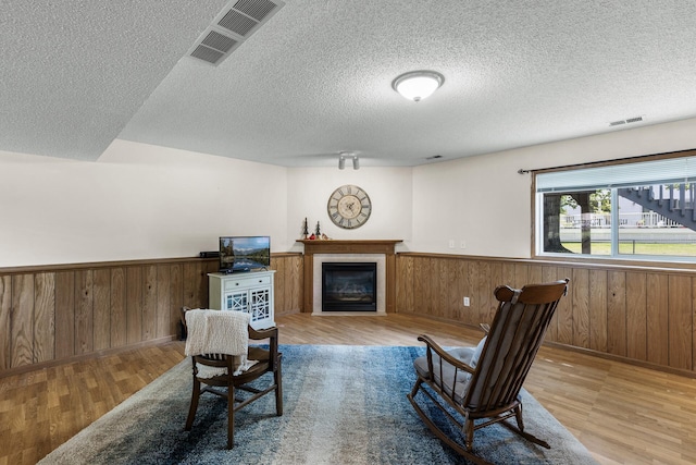 2294 Mathias Rd, Shakopee, MN 55379 - sitting room featuring wood finished floors, a textured ceiling, a wainscoted wall, a glass covered fireplace, and wood walls