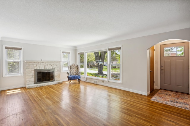 3511 Mckinley St NE, Minneapolis, MN 55418 - unfurnished living room featuring arched walkways, wood finished floors, a textured ceiling, baseboards, and a stone fireplace