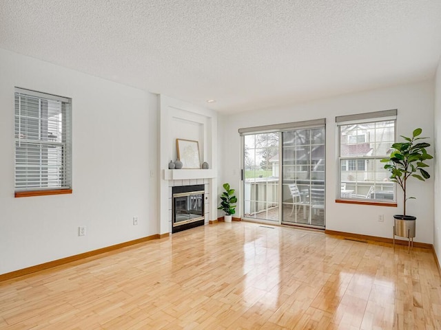 unfurnished living room featuring a textured ceiling, baseboards, a tiled fireplace, and light wood-style flooring