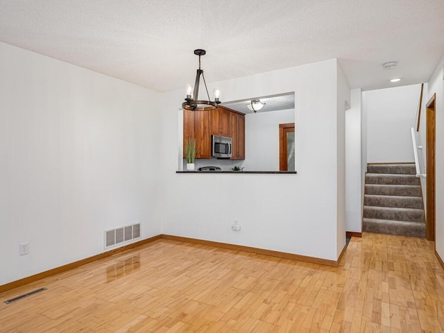 unfurnished dining area featuring visible vents, light wood-style flooring, baseboards, and a notable chandelier