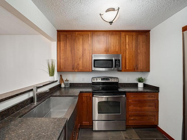 kitchen with a sink, a textured ceiling, appliances with stainless steel finishes, and brown cabinets